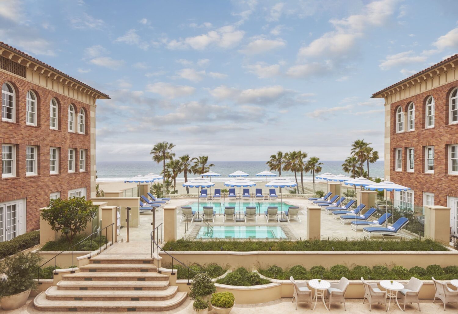 Beachfront hotel in Santa Monica with a pool, palm trees, and lounge chairs overlooking the ocean.